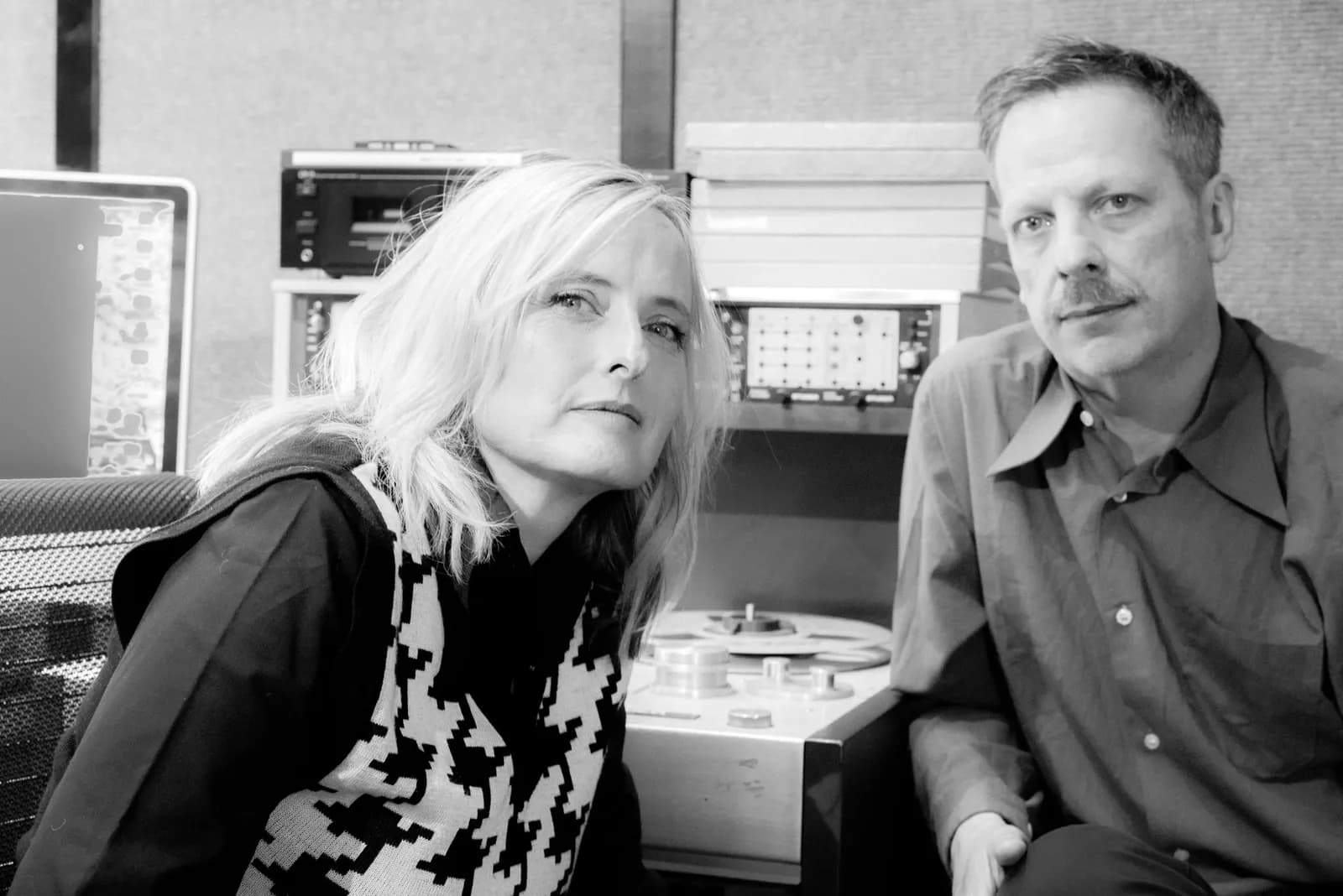A black and white portrait of a blonde woman and a man with a mustache sitting in front of sound recording equipment.